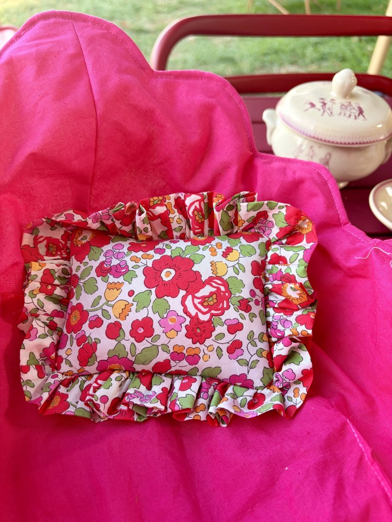Un petit coussin à motifs floraux avec un volant, posé sur un fond rose vif.