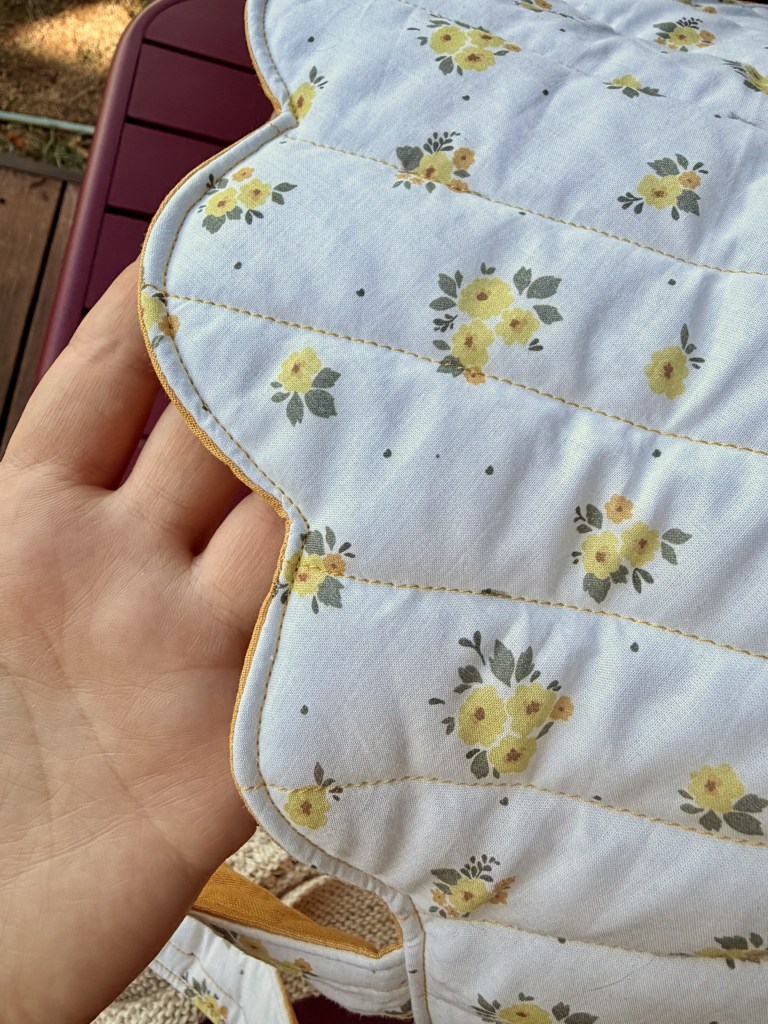 Gros plan sur un tissu matelassé avec un motif floral jaune et vert, tenu dans une main.