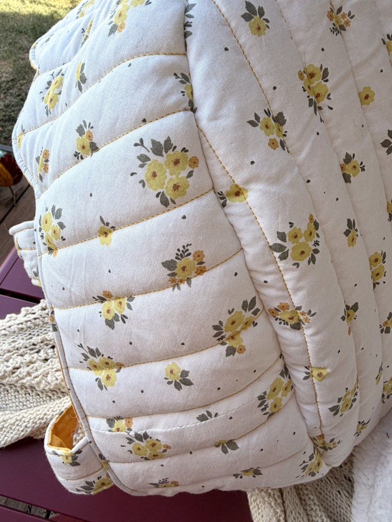 Un coussin matelassé avec un motif de fleurs jaunes et grises sur fond crème.