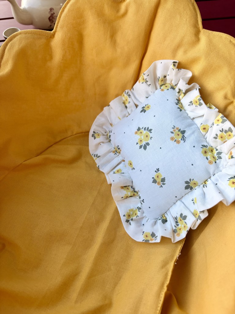Vue d'un coussin blanc à motifs floraux avec une bordure froncée, posé sur un tissu jaune uni.
