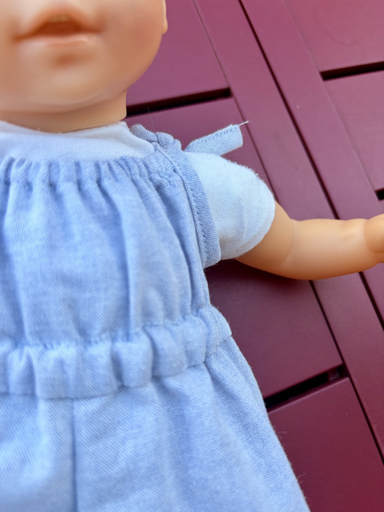 Détail du haut d'une poupée en robe bleu clair, posée sur un fond rouge.