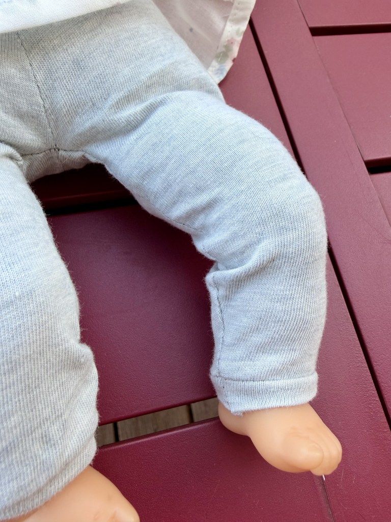 Un gros plan sur la jambe d'une poupée portant un pantalon gris, reposant sur une surface rouge.