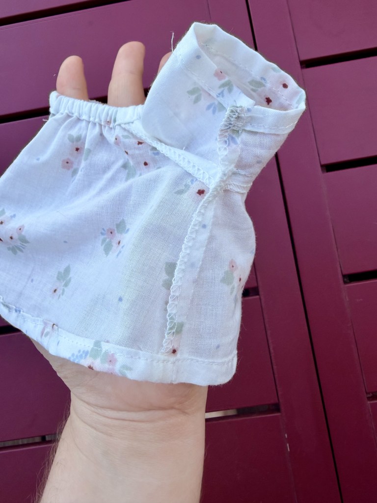 Une main tenant un petit morceau de tissu blanc à fleurs, avec une couture visible et un bord froncé.