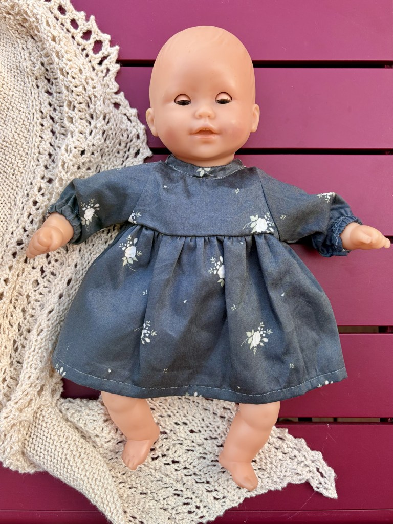 Une poupée en plastique avec une tenue à fleurs sur un fond de tricot beige.