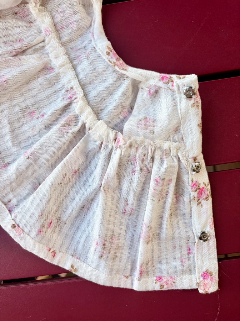 Détail d'un vêtement en tissu léger avec un motif à fleurs et des boutons sur le côté.